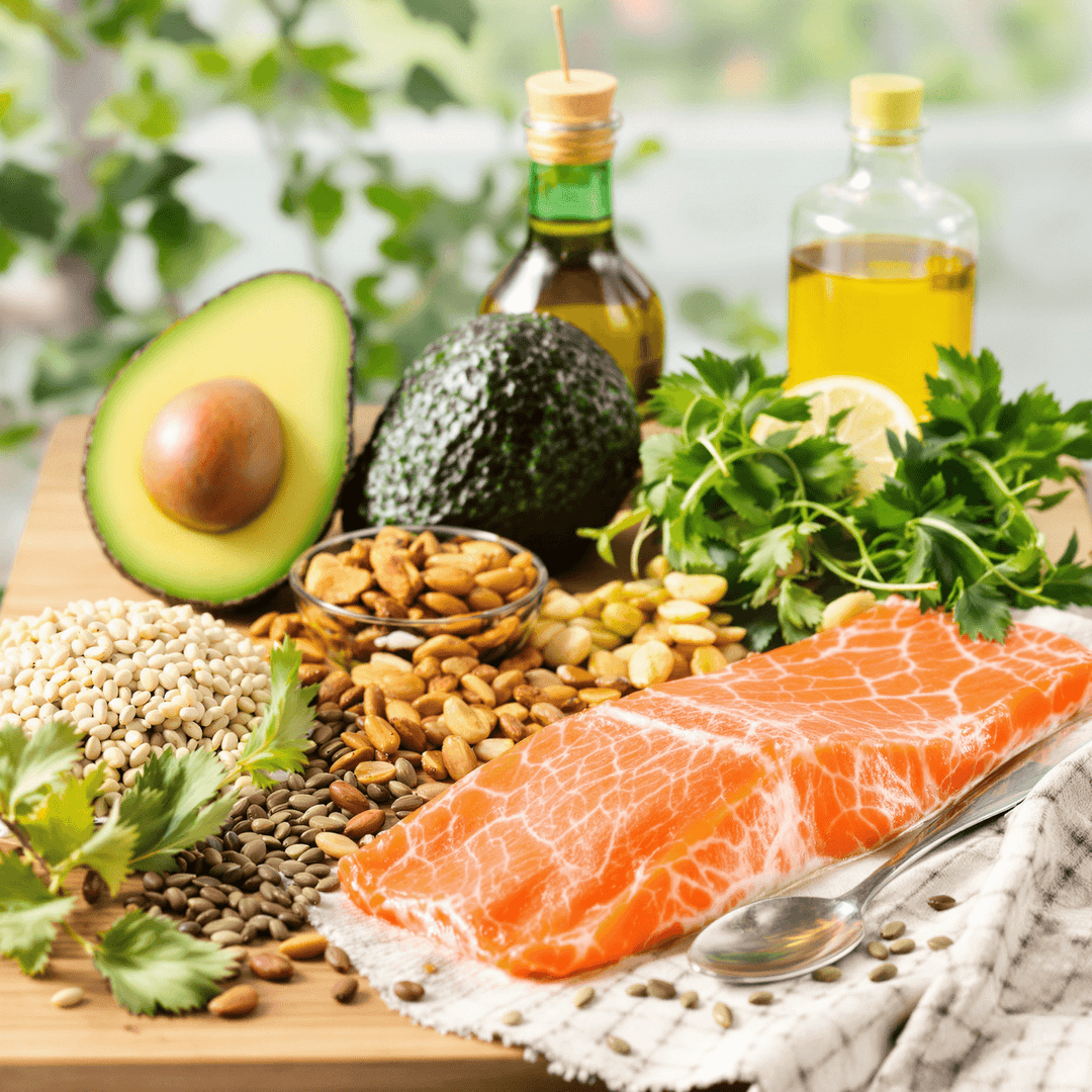 Close-up of healthy zero-carb foods including avocados, nuts, seeds, olive oil, and salmon on a wooden table with a bright background.