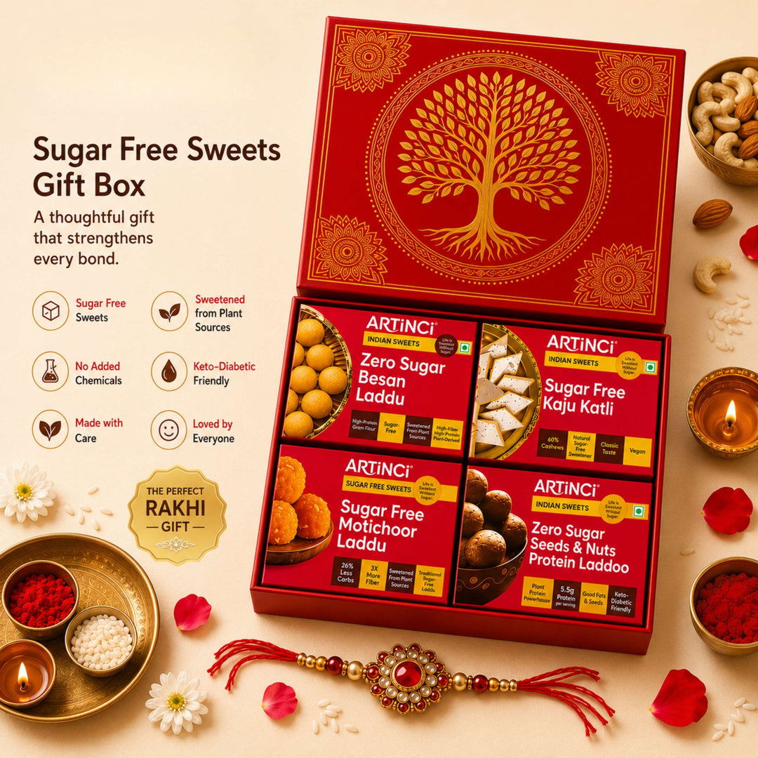 Artinci Sugar Free Sweets Gift Box set, featuring a red and gold gift box containing four varieties of sugar-free Indian sweets (Zero Sugar Besan Laddoo, Zero Sugar Kaju Kati, Zero Sugar Malai Laddoo, and Zero Sugar Seed & Nuts Laddoo). The box is styled on a warm beige background with festive props including a red and gold Rakhi, lit diya lamps, and decorative sweets.