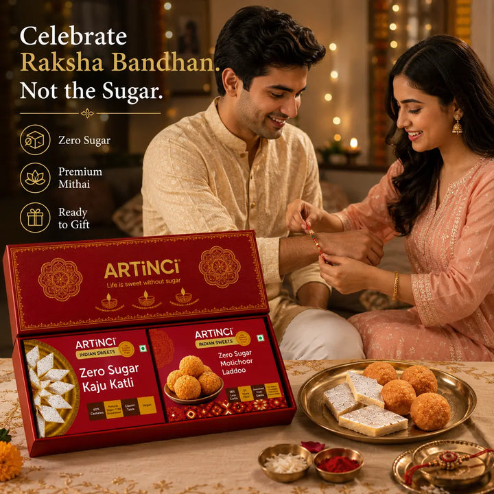 A man and woman in traditional Indian attire sit together in a warmly lit room, while an open red ARTINCI gift box of zero sugar Rajasthani laddoo and kaju kathi is displayed in the foreground with plates of sweets on a table. Text on the left reads 'Celebrate Raksha Bandhan.
