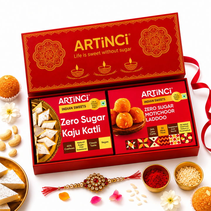 ArtINCI Zero Sugar Indian Sweets gift set in a red box, displayed with surrounding festive sweets, flowers, and a Rakhi on a white background.